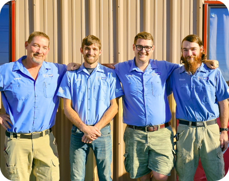 four employees wear blue button up shirts in front of a work van and warehouse