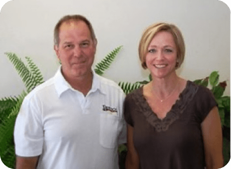 Tim and Stacey Bertsch stand in front of indoor plants facing the camera
